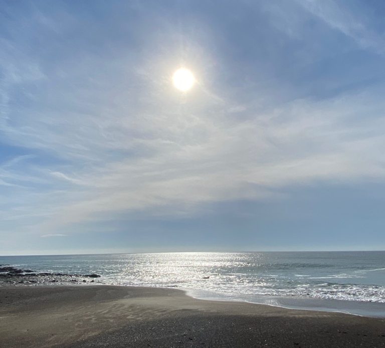 Bright sun shining over a calm ocean with gentle waves on a sandy beach.