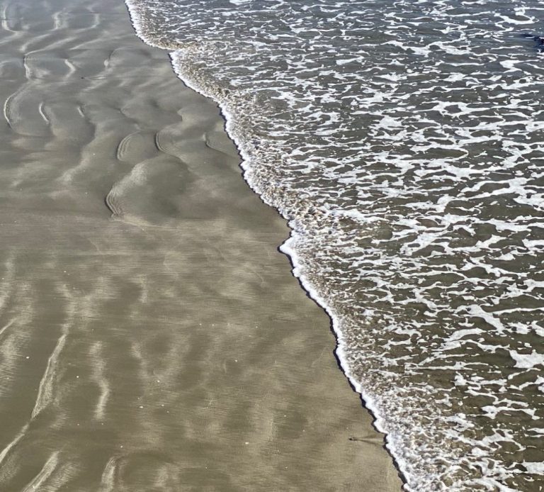 Gentle waves washing onto a sandy beach, creating rippled patterns.
